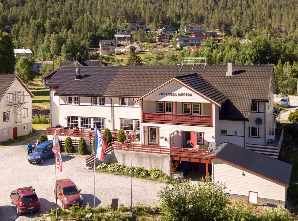 Lodge with multiple flags outside, situated in a forested area with cars parked.